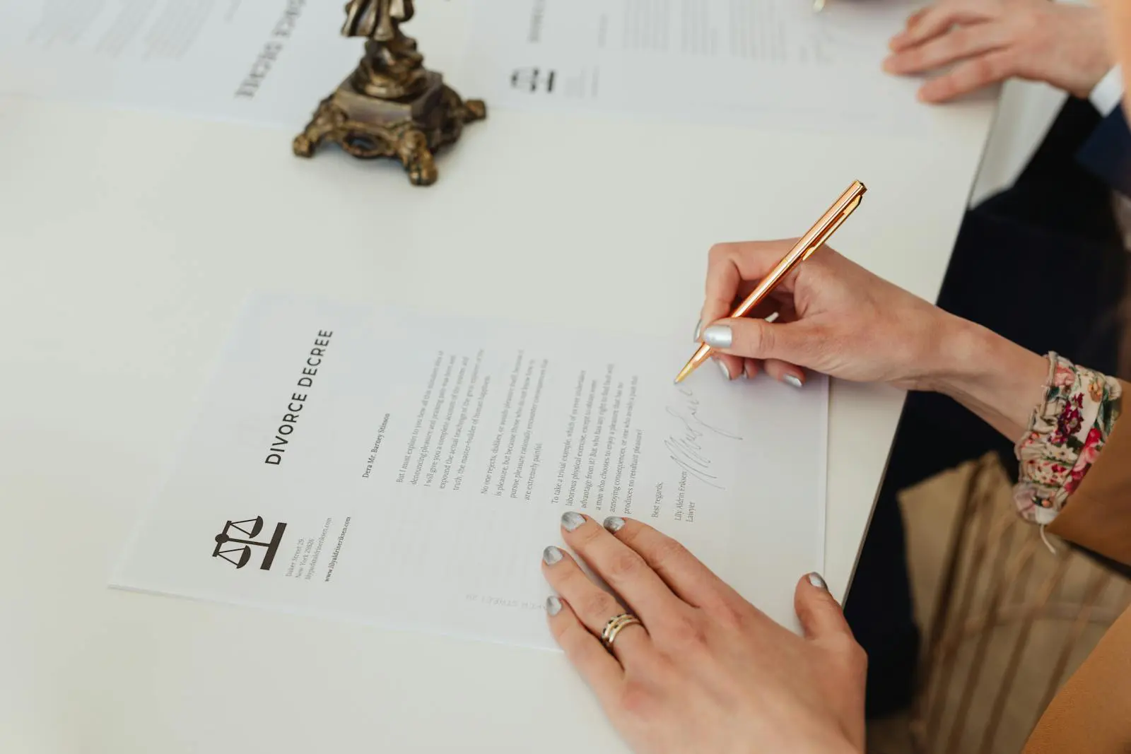 Photo by Photo By: Kaboompics.com Close-up of hands signing a divorce decree document on a desk, showcasing legal process.